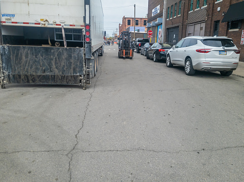 A loading truck and a hi-lo forklift  on a road in Eastern Market in Detroit, Michigan.Cars are parked on the street.