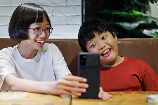 The adorable Asian siblings are having a fun time video calling their friends and family using a smartphone, staying connected with their loved ones through technology.