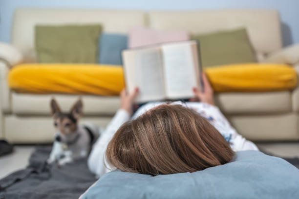 istock White woman lying on the floor while reading a book and resting next to her dog. 1495546374