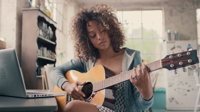 Attractive mixed race young girl learning to play guitar using laptop computer