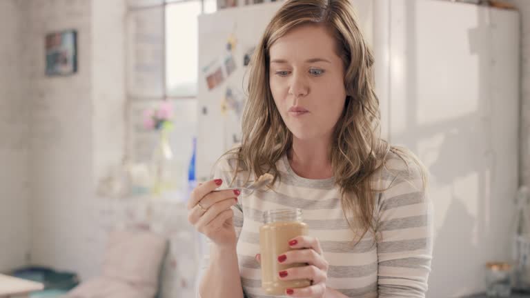 Caucasian girl indulging eating peanut butter from jar using spoon at home in the morning