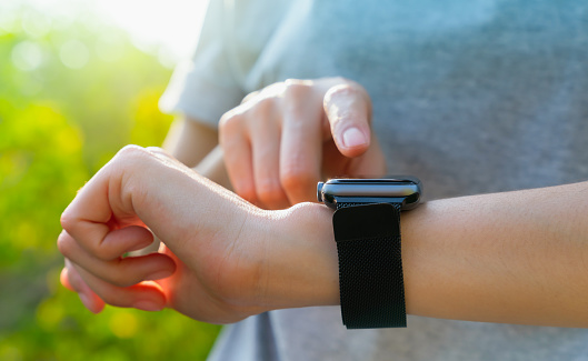 Hand wearing a smartwatch and checking active lifestyle and using fitness tracker outdoor.