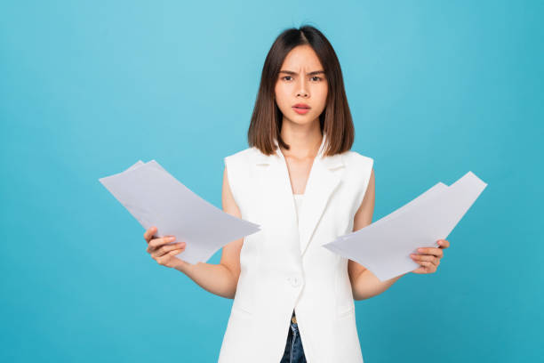 istock Boring young Asian woman holding document and stand on studio shot blue background. 1495553401