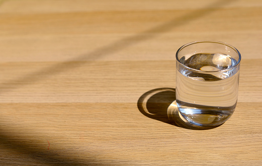 A glass of water on top of wooden table. The glass with fresh water on the wood table and sunlight.