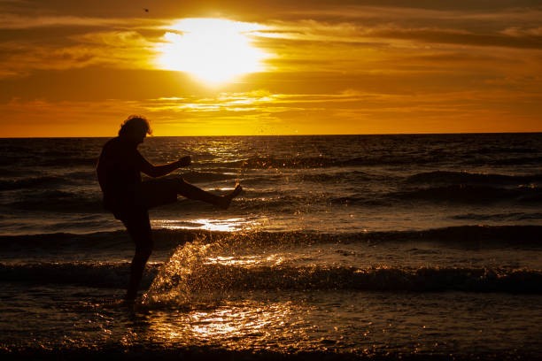 A man kicking water in the shore of the beach during a sunset stock photo