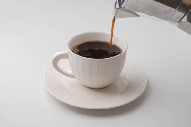 istock Hand holding Mokapot pouring coffee into white cup on table. Black coffee in white cup isolated on white background 1495560523
