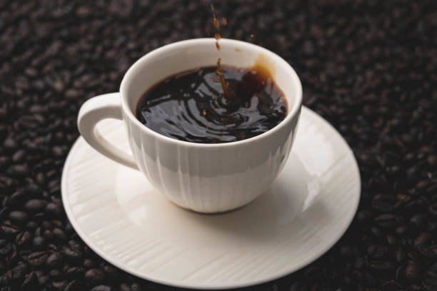 istock Hand holding Mokapot pouring coffee into white cup on table. Black coffee in white cup isolated on background of roasted coffee beans. 1495560545