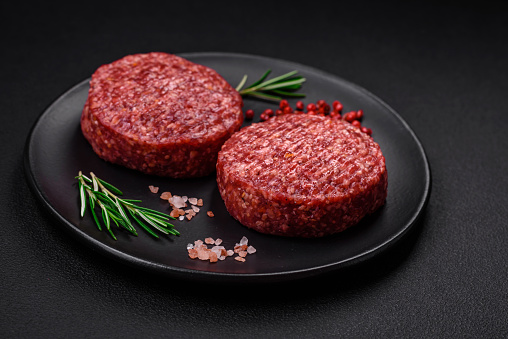 Fresh raw ground beef burger patty with salt and spices on textured concrete background