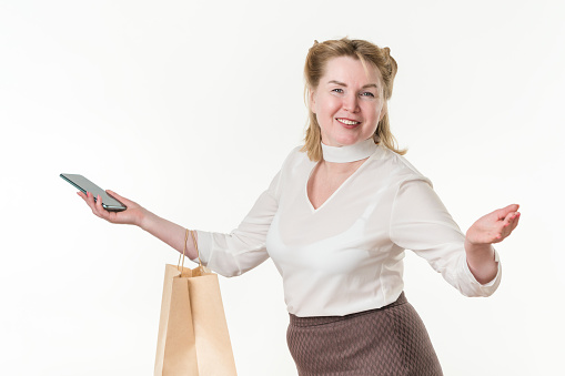 Waist up photo of happy woman with shopping paper package bags and mobile phone. Caucasian ethnicity blonde female 49 years old smiling and looking at camera. Concept of shopping and consumerism. Part of series