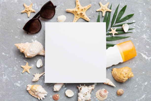 istock Summer time concept with blank greeting card and blank white paper on colored background. Seashells from ocean shore in the shape of frame separated with space for text top view 1495565160