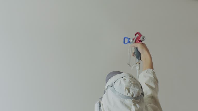 Worker painting the wall by airless spray gun with white color. Airless spray painting. Repair at home or office.