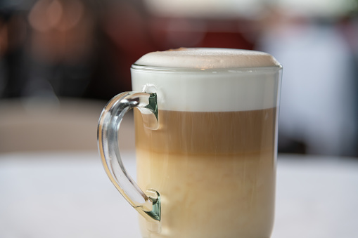 Close-up view of latte macchiato coffee drink standing on white table in restaurant. Soft focus. Hot drinks theme.