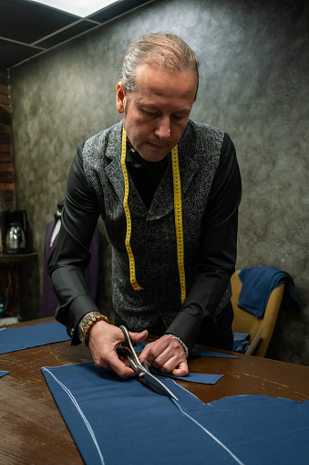 fashion designer is cutting cloth fabric on the table clippers are in men hand focus on foreground vertical still