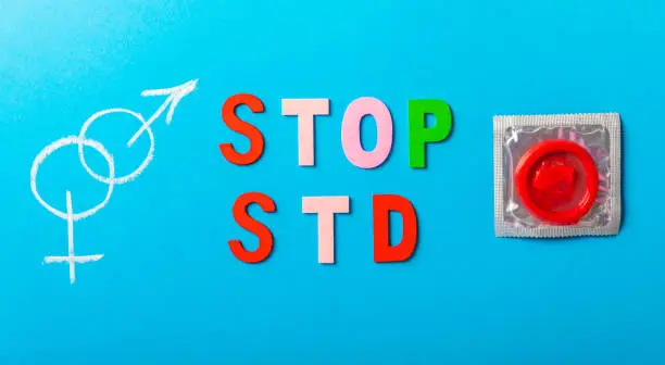 Colorful blocks with "STOP STD" phrase background, flat lay. Super safe strawberry condoms with a pleasant smell on a blue background. Contraceptives are made from natural rubber latex, high