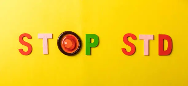 Colorful blocks with "STOP STD" phrase background, flat lay. Super safe strawberry condoms with a pleasant smell on a yellow background. Contraceptives are made from natural rubber latex, high