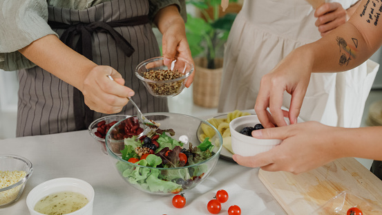 Closeup of young Asian women friends preparing vegetarian and cooking salad in kitchen table at home. Lifestyle healthy food eating enjoying natural life and plant-based diet concept.