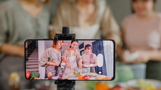 Closeup young Asian women friends vlogger online influencer recording video content cooking salad in kitchen at home. Lifestyle healthy food eating enjoying natural life and plant-based diet concept.