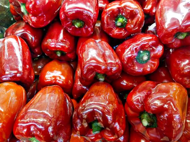 Red bell pepper isolated against a black background. Vegetables artfully presented. Close up of a nutritious paprika. Shadow play on a dark background. Ribbed surface. Bright red spot in the dark.