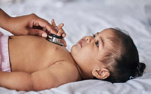 Healthcare, stethoscope and sick baby on a bed for a consultation in a children medical clinic. Infant girl kid with a cold, flu or illness getting a wellness examination or checkup at the hospital.