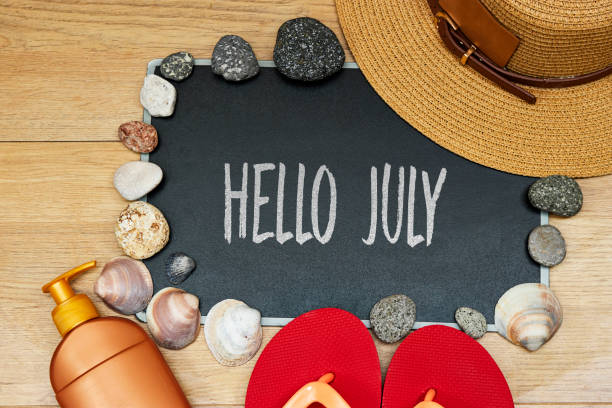 istock summer concept, sun cream and slipper with hello July text on chalkboard and stones. seashell hat on wood table 1495579764