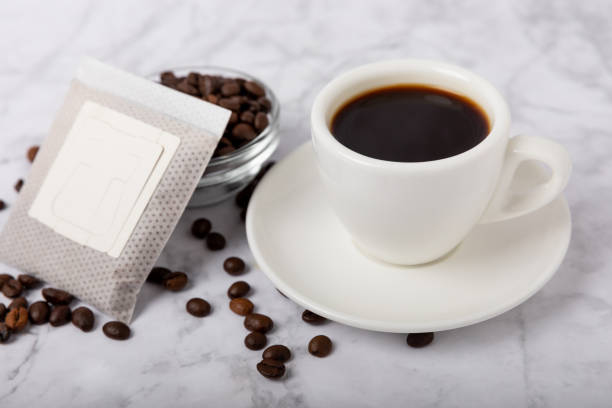 istock Drip coffee bags, coffee beans and a white cup on a texture table. Ground coffee for brewing in a cup, paper bag drip coffee filter packaging. Place to copy. Place for text. 1495581049