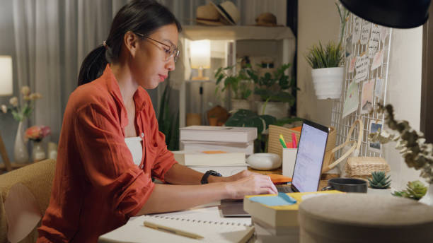 istock Young Asian woman wear casual sit front of desk with computer laptop and think create on work idea in living room at house at night. Work from home. 1495581906