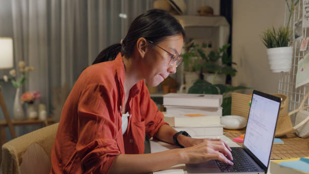 istock Young Asian woman wear casual sit front of desk with computer laptop and think create on work idea in living room at house at night. Work from home. 1495581930