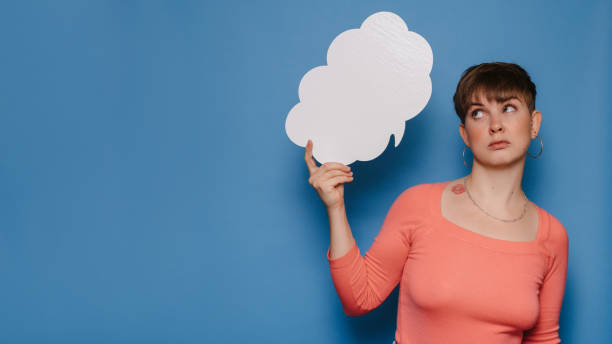 istock Studio shot of a young woman with a puzzled expression, holding a white empty banner in the form of a cloud on a blue background. Copy space, space for your ad or text. 1495593716