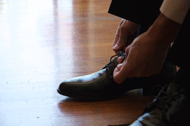 Elegant man laces up sartorial leather shoes, male dressing marriage suit