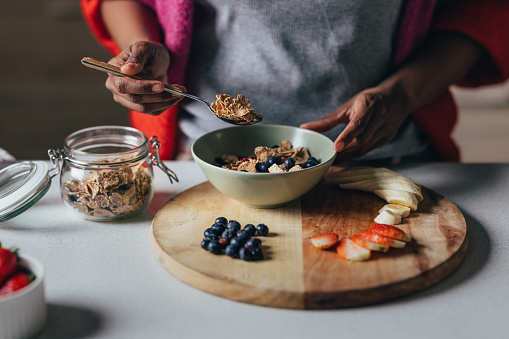 Morning routine: A close up view of an unrecognizable African-American female making a vegetarian meal with fresh organic fruits and a few spoons of cereals.