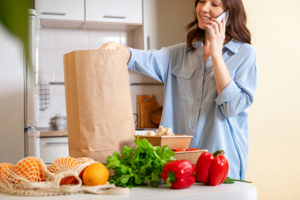 istock Young woman checking her fresh groceries delivery ordered from internet. Fresh organic vegetables, greens and fruits. Kitchen interior.  Food delivery concept 1495599822