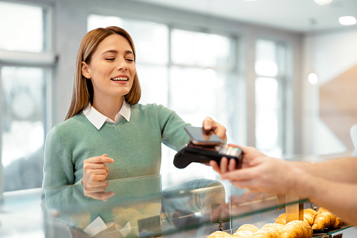 Caucasian woman paying at a bakery shop with her smartphone at the checkout counter
