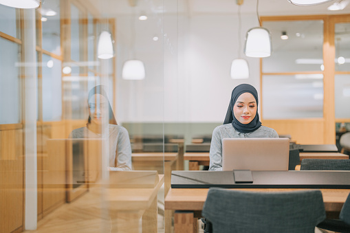 Asian Muslim Woman typing on laptop in co-sharing office