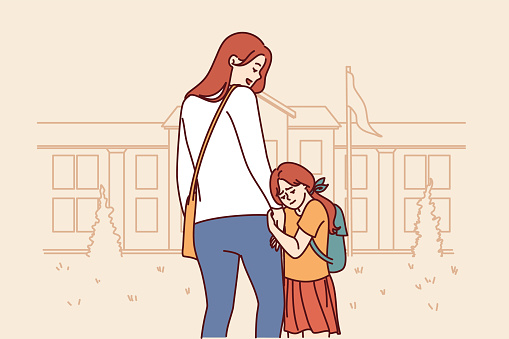 Mom accompanies daughter in elementary school, supporting or motivating girl standing near building of educational institution. Little girl feels attached to mother and does not want to go in school