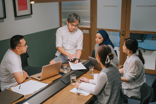 Asian Chinese man leading meeting briefing multiracial colleagues together in boardroom. Creative team, casual business coworker, in project meeting at modern office. Startup teamwork