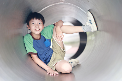 Young boy is having fun at the playground inside slide tube.