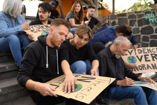 istock Group of focused diverse protesters creating carton placards while sitting on stairs during preparation for strike 1495621173