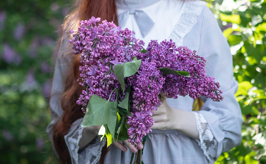 young girl with long red hair with a wreath of lilacs on her head in the garden in spring