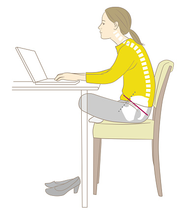 A woman who does desk work in a stooped and cross-legged posture