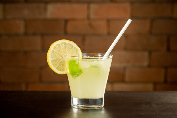 Glass of lime caipirinha drink on top of table in front of a brick wall with text space stock photo