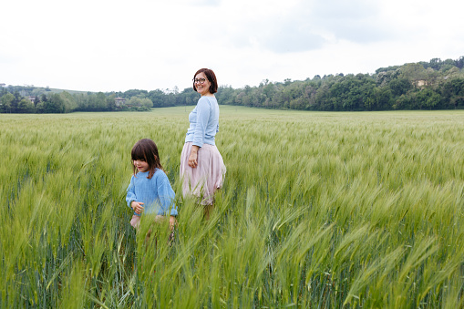 smiling mother and daughter in pink skirt standing in the field of wheat