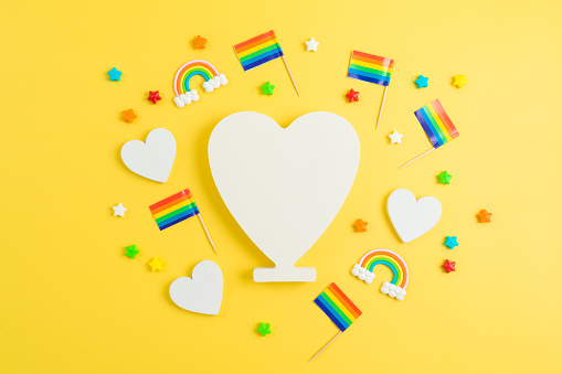 LGBTQ pride month concept with rainbow flag and heart shape on yellow background. Top view, flat lay