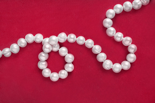 String of white pearl necklace on red background closeup