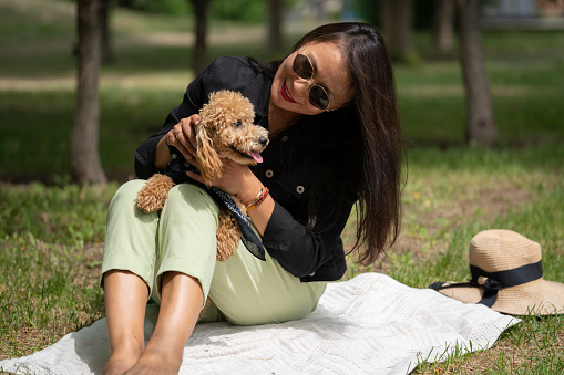 A beautiful Asian girl (Kazakh) holds a dog (mini poodle) in her hands. The girl has emotions of happiness and joy on her face.