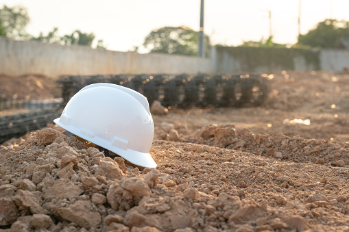 A white safety hardhat helmet is placed on dirt ground at the construction work site, unsafe workplace. Safety PPE object photo.