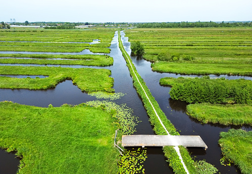 Beautiful aerial view of a small path in the wide open Dutch polder landscape with water filled ditches and canals.
