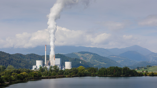 Smoking chimney at thermal power plant near lake and green nature.