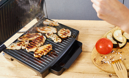 Electric grill with meat and spices on cutting board. Electric stove on a modern kitchen.
