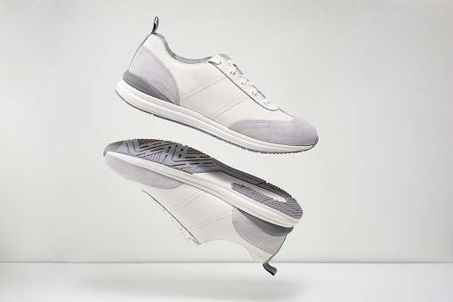 Pair of stylish sports sneaker levitating on light background. Fashion shoes in the air. Creative footwear concept.