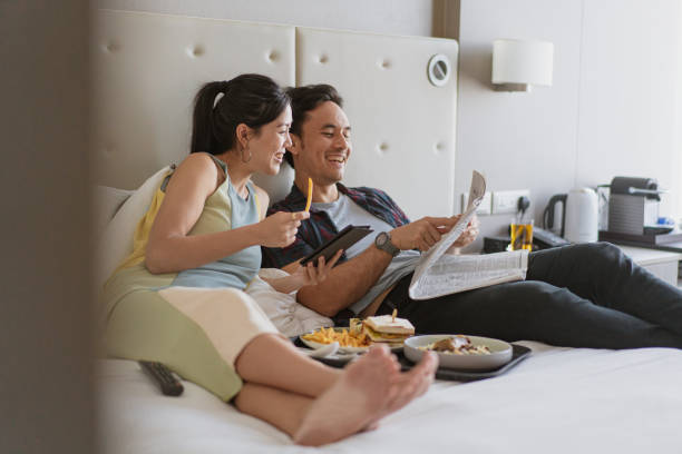 休日の楽しみ – ルームサービスとベッドでの朝食を楽しむアジア人夫婦 - honeymoon hotel hotel suite hotel room ストックフォトと画像